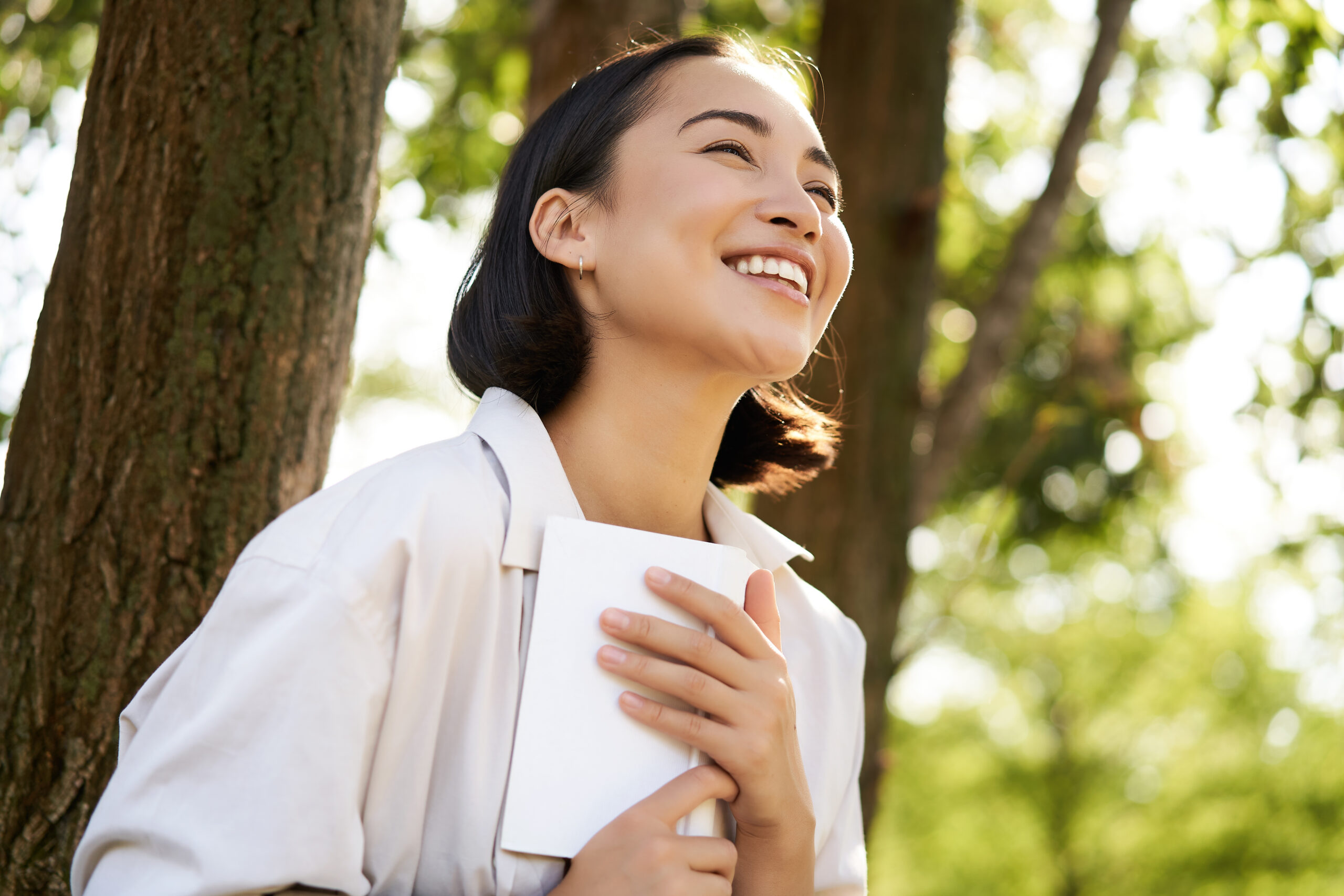 Romantic smiling girl reading book in park or foret, sitting under tree shade on sunny day, relaxing on fresh air surrounded by nature Romantic smiling girl reading book in park or foret, sitting under tree shade on sunny day, relaxing on fresh air surrounded by nature.